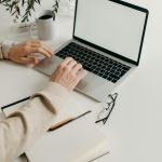 A clean and modern workspace featuring a laptop, houseplant, and notebook.