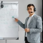 Asian man in a gray suit giving a presentation with a flipchart, wearing a headset.